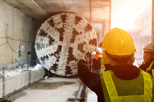 Engineer wear yellow helmets,vests  safety are discussing.Technician control underground tunnel construction at working shaft.Transport pipeline by Tunnel Boring Machine(TBM) method for electric train