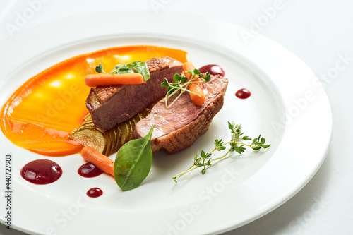 Appetizing confit duck breast with pear and yellow apple puree, berry sauce in a white plate. Isolated on grey background.