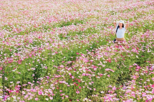 Asian beautiful young woman walking and take photo in Cosmos flower field landscape background.Concept of travel in summer season at Thailand.