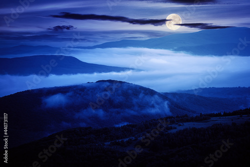 glowing fog in the rural valley at night. beautiful mountain landscape in full moon light. view from the hill © Pellinni