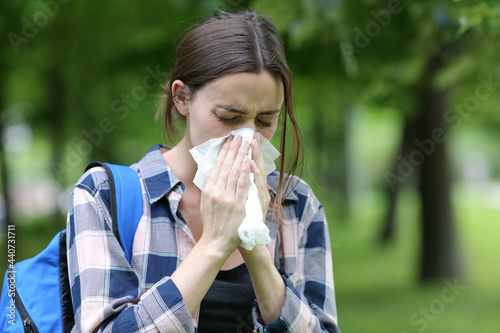 Student blowing on tissue in a park