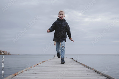 A happy boy runs down the pier from his dad on a cold autumn day