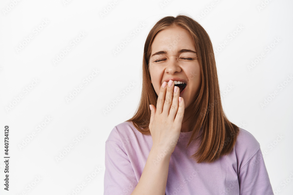 Close up of young woman yawning, student tired during exams, waking up early, covering opened mouth bored, standing exhausted against white background Close up of young woman yawning, student tired during exams, waking up early, covering opened mouth bored, standing exhausted against white background