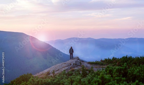 The traveler looks at the stunning view of the snow-capped mountains at sunset. Young man with a backpack and tourist equipment is hiking in the national park in winter, engaged in extreme sports. © Zhanna