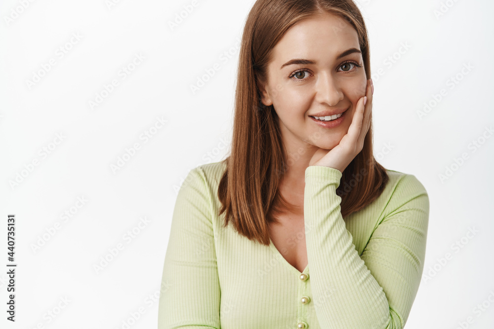 Beauty and women. Close up of beautiful and feminine girl touching her clean, natural facial skin, gently touch face and smile tender at camera, white background Beauty and women. Close up of beautiful and feminine girl touching her clean, natural facial skin, gently touch face and smile tender at camera, white background