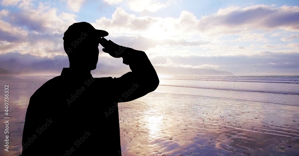 Fototapeta premium Composition of male soldier saluting over sea and blue sky