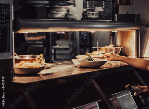 A food waiter picks up a plate from a food serving counter. The plates and bowls under the light are waiting