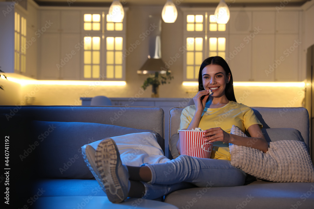 Obraz premium Young woman watching movie with popcorn on sofa at night, space for text