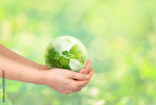 Hand holding globe glass world ball with green grass field in side the globe glass on nature blur background. eco concept