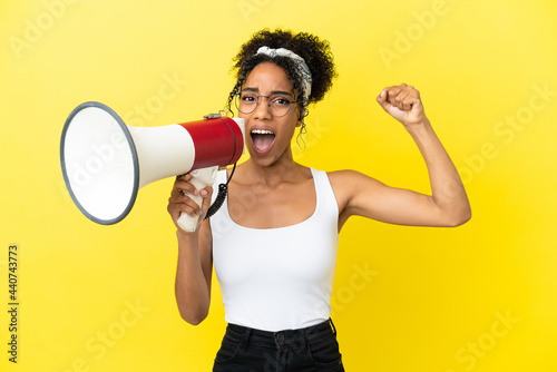 Young african american woman isolated on yellow background shouting through a megaphone to announce something