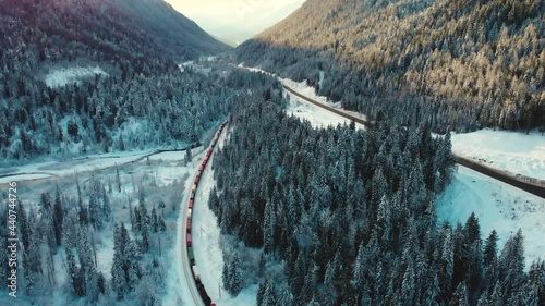 Long Industrial Train Passing By Forest Covered With Snow At Glacier National Park In Winter. - aerial
 photo
