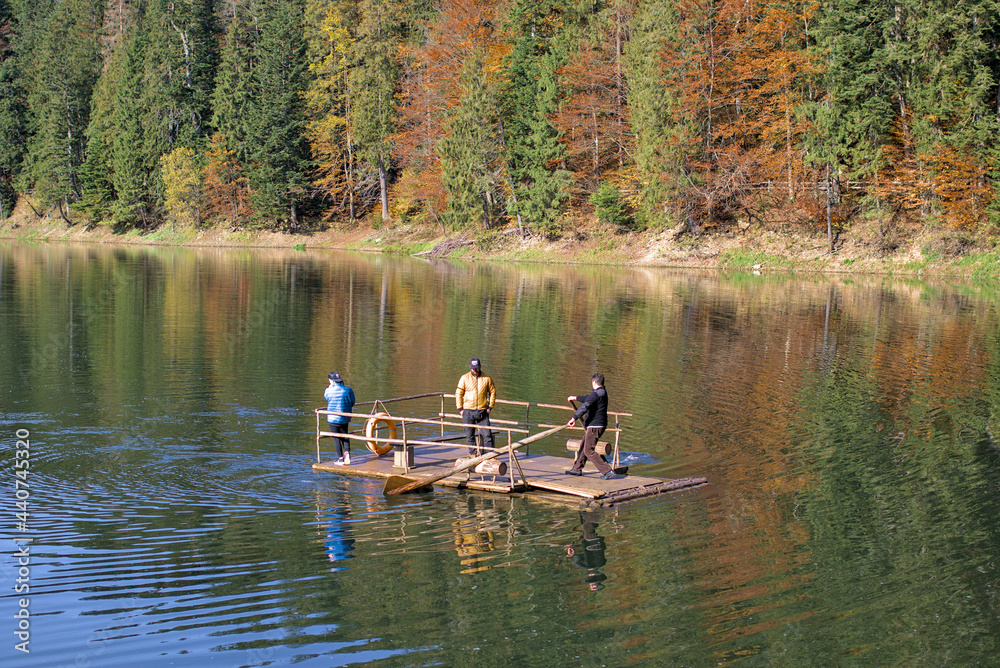 Zakarpattia Oblast, Ukraine - October 28, 2020: People are sailing on a raft on a picturesque lake in the autumn forest. Mirror reflection of a spruce forest. Mountain Lake Synevyr in Carpathian.