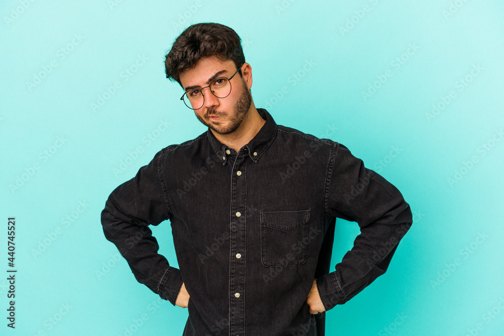 Young caucasian man isolated on blue background frowning face in displeasure, keeps arms folded.
