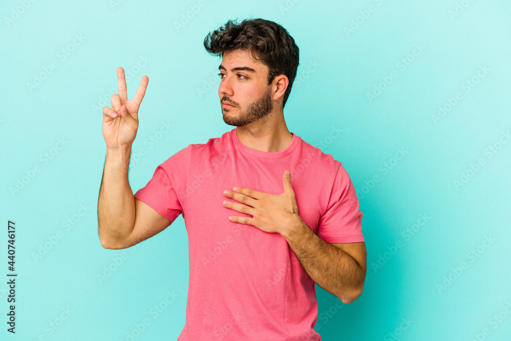 Fototapeta premium Young caucasian man isolated on blue background taking an oath, putting hand on chest.