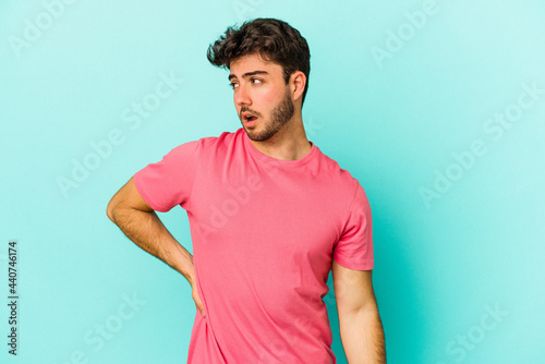 Young caucasian man isolated on blue background suffering a back pain.