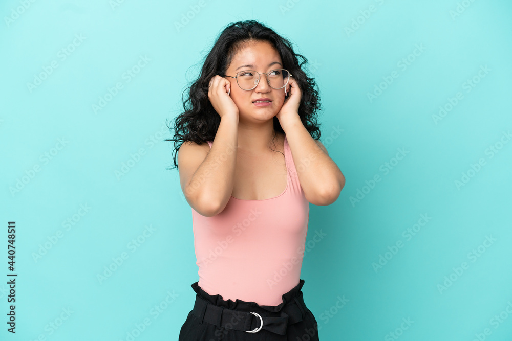Young asian woman isolated on blue background frustrated and covering ears