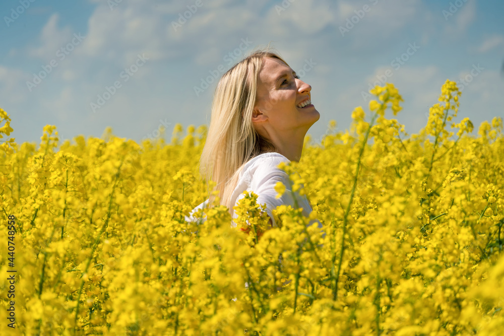 Happy smiling young blonde woman in a white shirt in a rapeseed field with her arms spread out to the side on a sunny day Happy smiling young blonde woman in a white shirt in a rapeseed field with her arms spread out to the side on a sunny day
