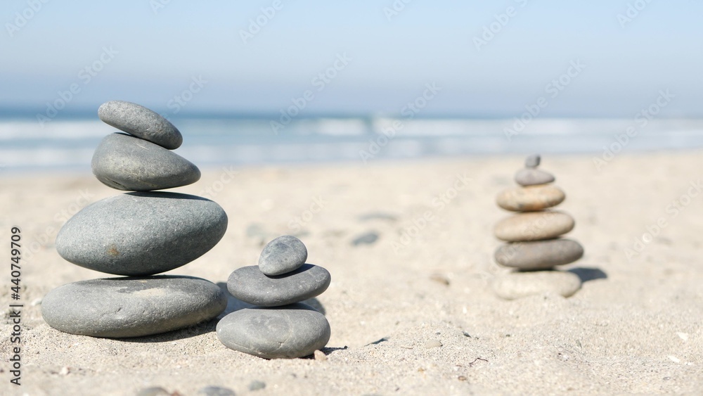 Fototapeta premium Rock balancing on ocean beach, stones stacking by sea water waves. Pyramid of pebbles on sandy shore. Stable pile or heap in soft focus with bokeh, close up. Zen balance, minimalism, harmony and peace