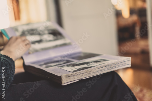 Close-up of a girl in dark clothes sitting on the sofa, holding an album on her lap and looking at old photos