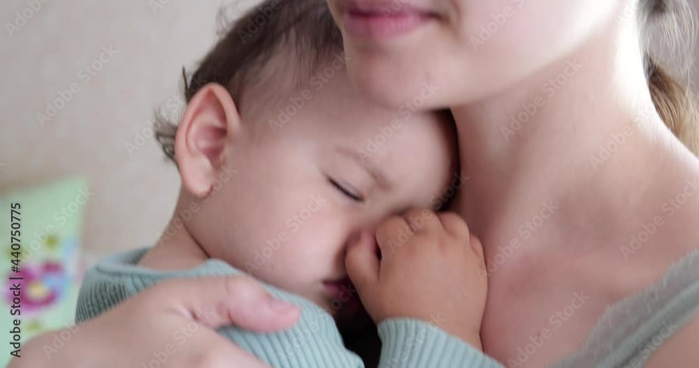 mother holds her sleeping baby son at home and rocks him. boy sleeping in his mother arms mother holds her sleeping baby son at home and rocks him. boy sleeping in his mother arms