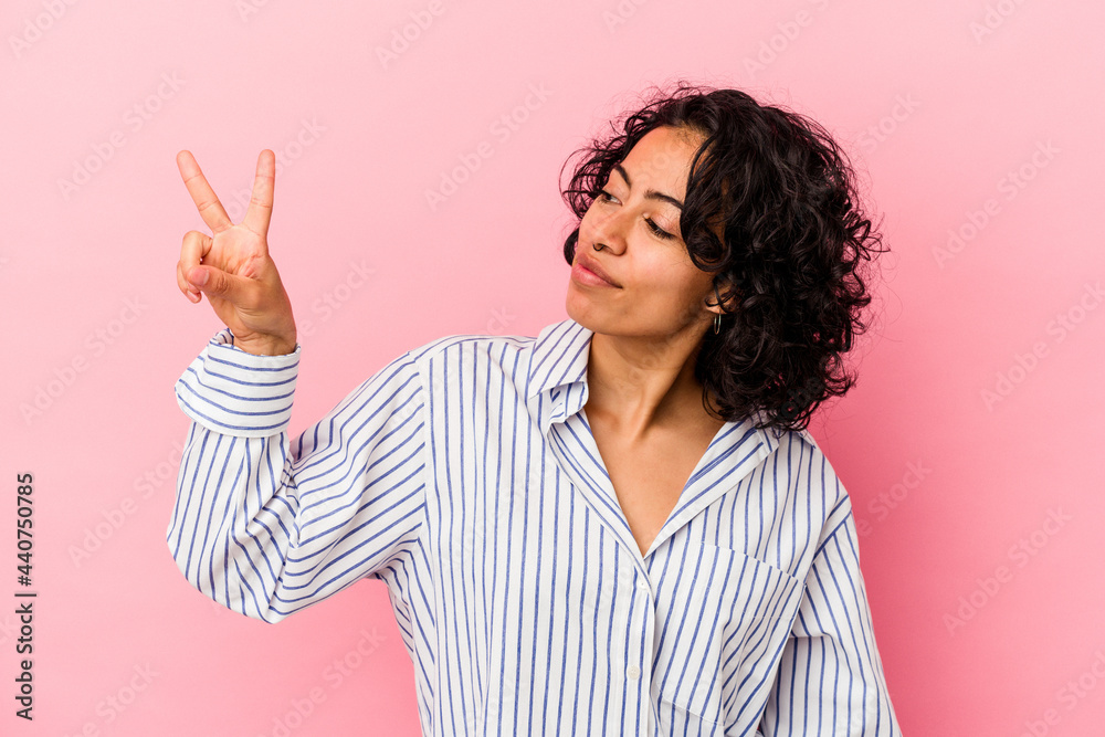 Young curly latin woman isolated on pink background joyful and carefree showing a peace symbol with fingers. Young curly latin woman isolated on pink background joyful and carefree showing a peace symbol with fingers.