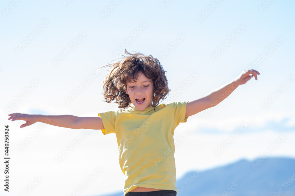 smiling boy with long hair jumps and has fun playing with open arms. blue sky background on a sunny day smiling boy with long hair jumps and has fun playing with open arms. blue sky background on a sunny day