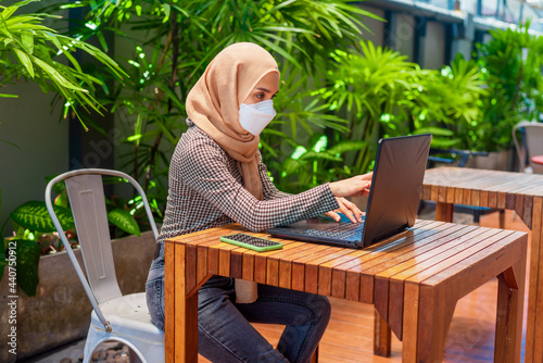 Muslim business woman in medical mask with laptop. Working on line at home.