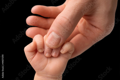 Father holding newborn baby's fingersnewborn . Hand of a newborn baby. Hands of parents and baby closeup. Black studio background. 