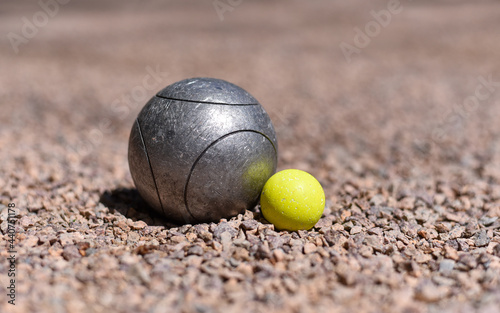 A petanque ball (boule) close to a yellow jack target ball on a pink gravel petanque ground.
