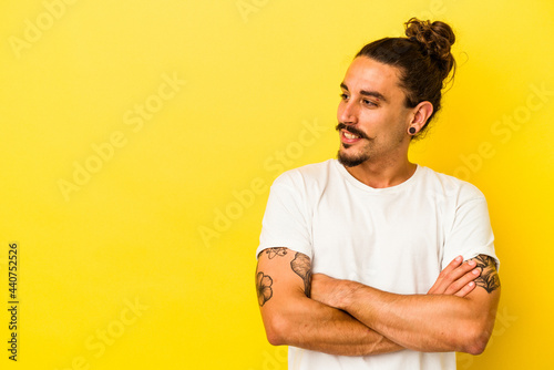 Young caucasian man with long hair isolated on yellow background smiling confident with crossed arms.