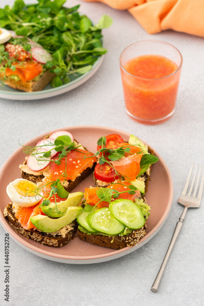 Healthy tasty breakfast, sandwiches with avocado and salmon, cucumbers and tomatoes, radishes and microgreens of peas with boiled egg and root salad, grapefruit smoothie in a glass
