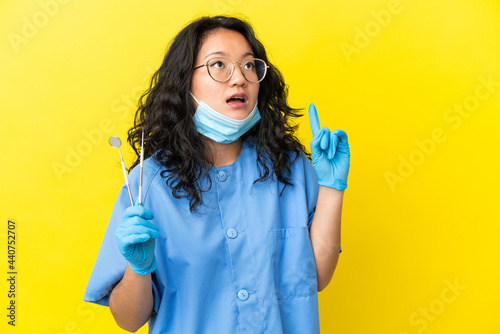 Young asian dentist holding tools over isolated background thinking an idea pointing the finger up