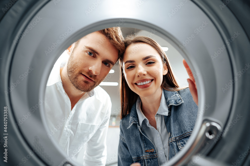 Fototapeta premium Happy couple choosing new washing machine in a store, view from the inside of washing machine