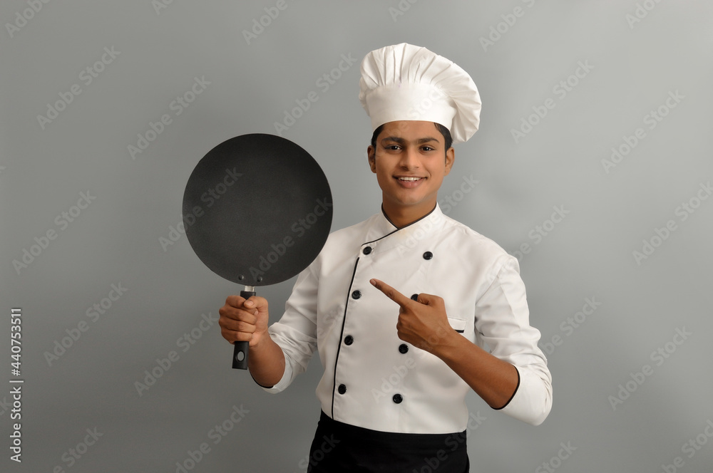 Confident smiling successful Indian chef holding a frying pan and pointing, profession and people concept Confident smiling successful Indian chef holding a frying pan and pointing, profession and people concept