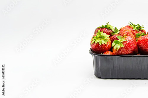 Strawberries in a dark plastic container against white background. Sweet and beautiful berry in a plastic container. Strawberries for sale.