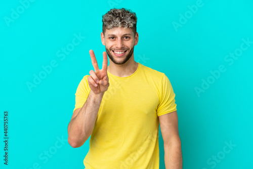 Young handsome caucasian man isolated on blue background smiling and showing victory sign