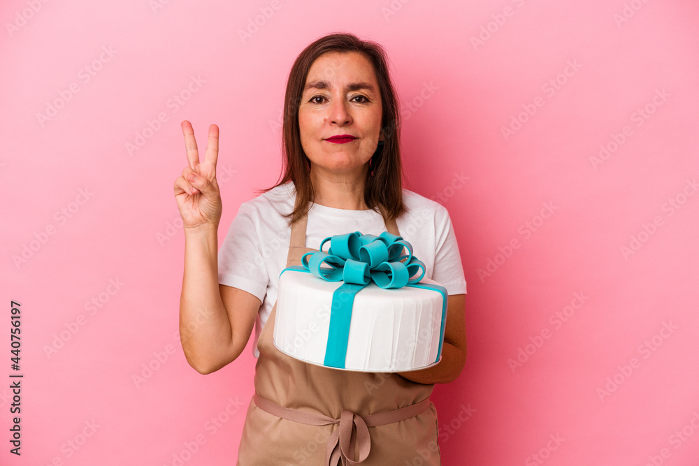 Middle aged pastry chef woman holding a cake isolated on blue background showing number two with fingers. Middle aged pastry chef woman holding a cake isolated on blue background showing number two with fingers.