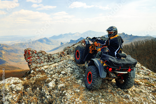 Man in helmet sitting on ATV quad bike in mountains photo