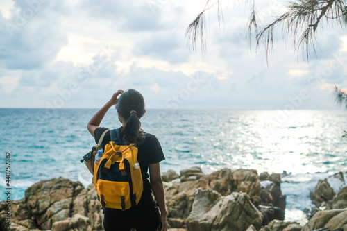 A young female traveler with a backpack on a cliff on the sea, stands with her hands up. The concept of travel, freedom.