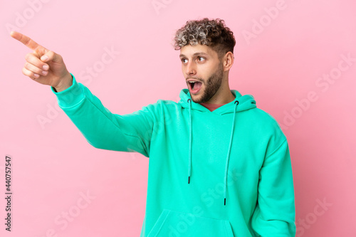 Young handsome caucasian man isolated on pink background pointing away © luismolinero