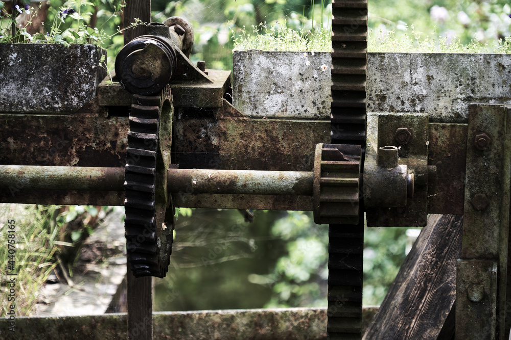 Old rusty, gears and racks on the gearbox of a historic weir at the outlet of a stream next to a watermill, dark, desaturated atmosphere