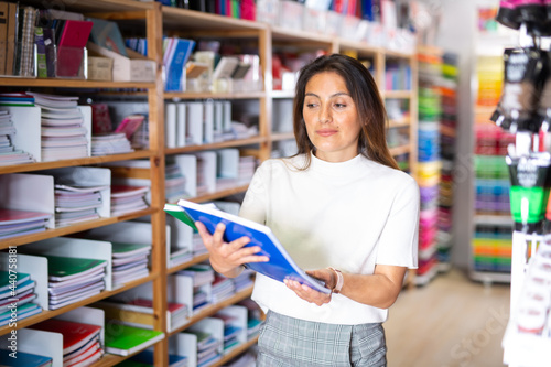Latino woman with notebooks stands next to shelves of the stationery store