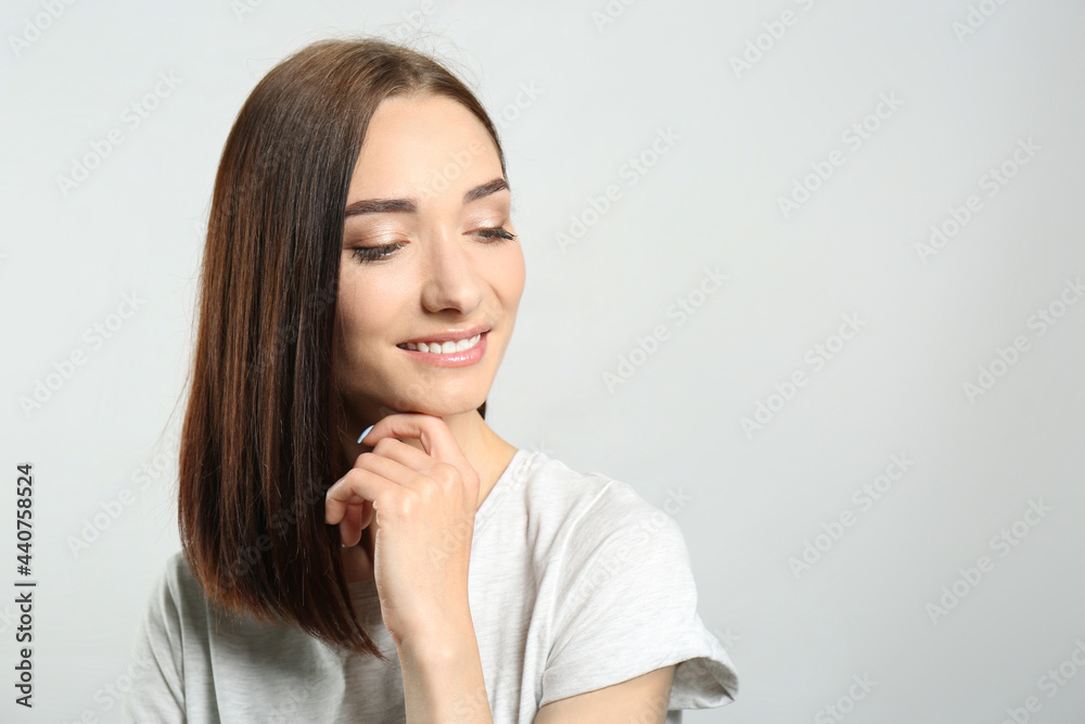 Portrait of pretty young woman with gorgeous chestnut hair and charming smile on light background, space for text Portrait of pretty young woman with gorgeous chestnut hair and charming smile on light background, space for text