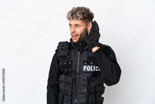 SWAT caucasian man isolated on white background listening to something by putting hand on the ear