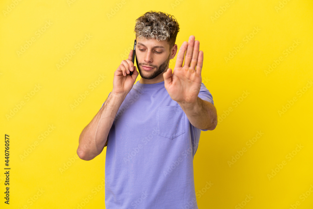 Young caucasian man using mobile phone isolated on yellow background making stop gesture and disappointed Young caucasian man using mobile phone isolated on yellow background making stop gesture and disappointed