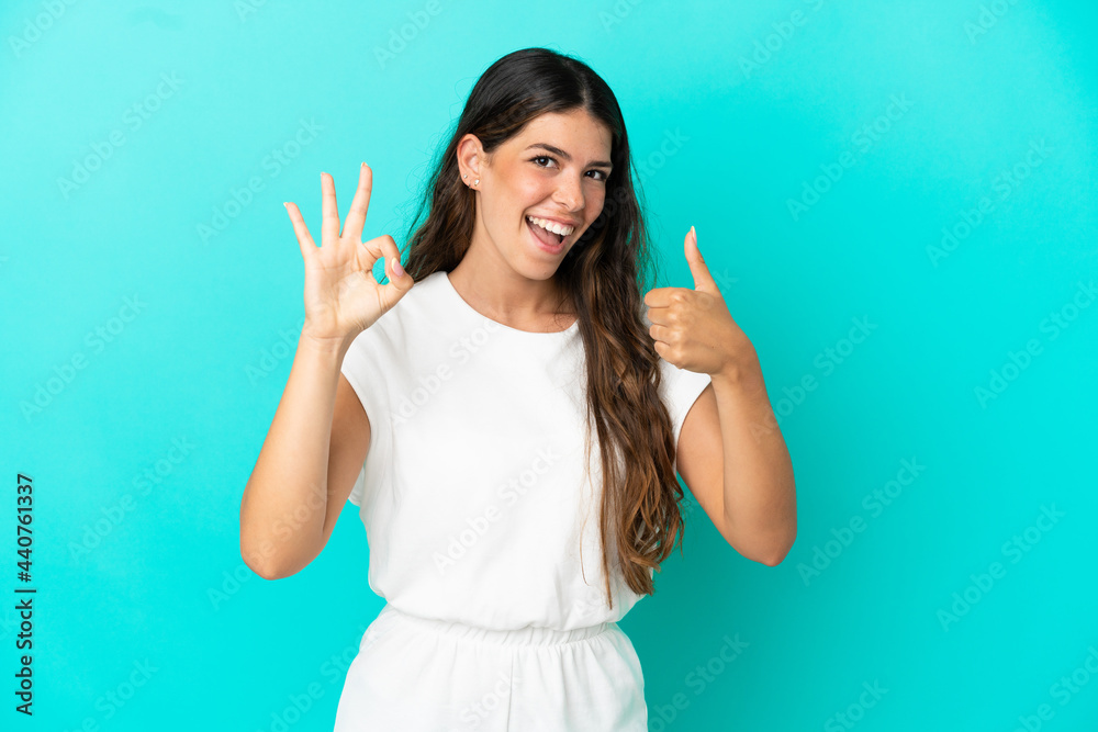 Young caucasian woman isolated on blue background showing ok sign and thumb up gesture Young caucasian woman isolated on blue background showing ok sign and thumb up gesture