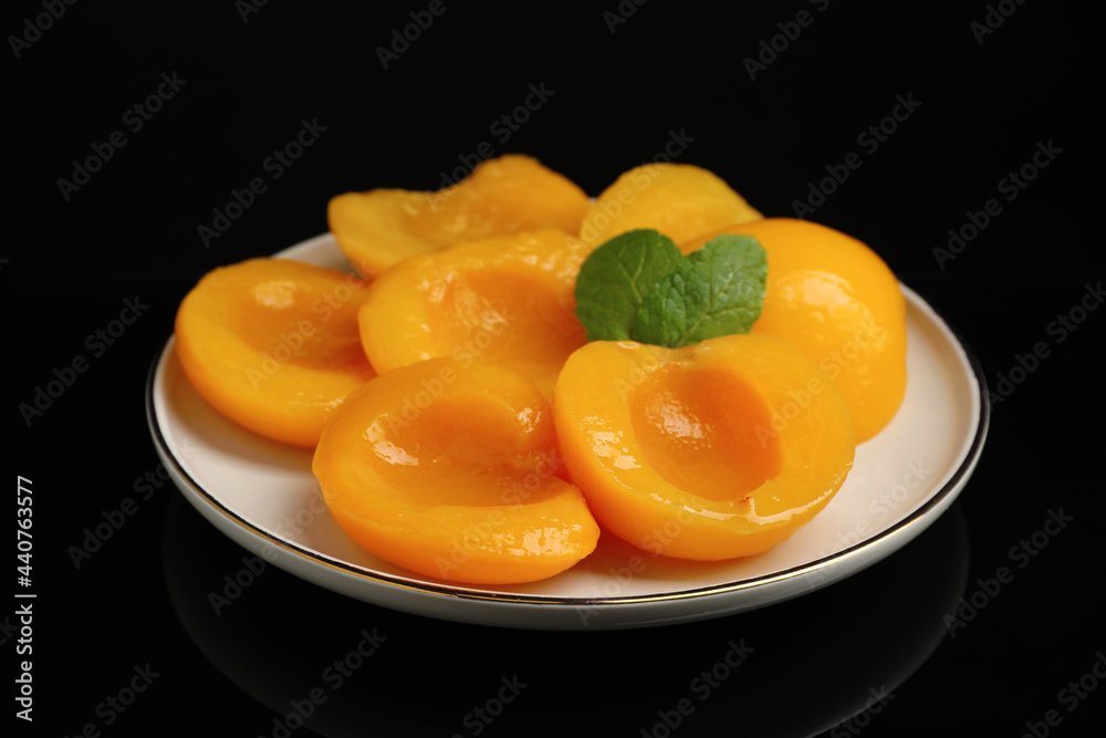 Plate with canned peach halves on black background Plate with canned peach halves on black background