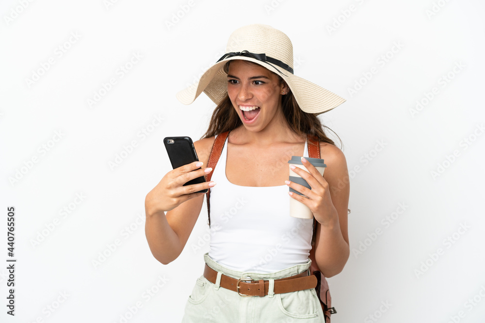 Young caucasian woman wearing a Pamela in summer holidays isolated on white background holding coffee to take away and a mobile Young caucasian woman wearing a Pamela in summer holidays isolated on white background holding coffee to take away and a mobile