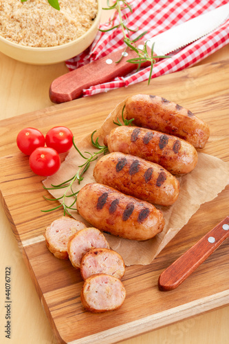 Linguicinha de frango assada sobre a mesa ainda espeto, farofa, tomate acompanham.