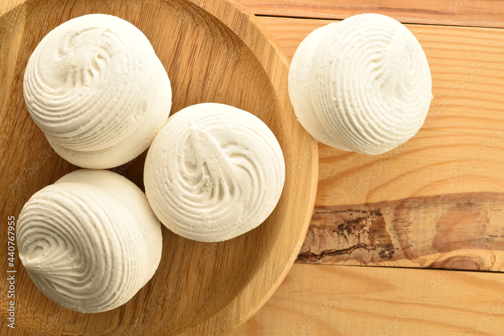 Several white sweet marshmallows on a round bamboo tray on a wooden table, close-up, top view. Several white sweet marshmallows on a round bamboo tray on a wooden table, close-up, top view.